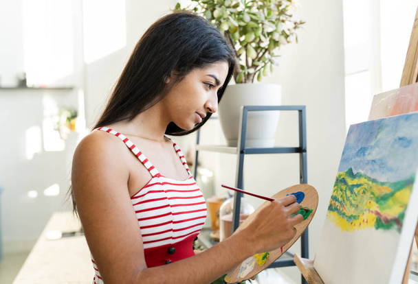 Young brunette hindu woman painting a oil paint picture at home. Millennial indian female at home. - Foto, Imagen