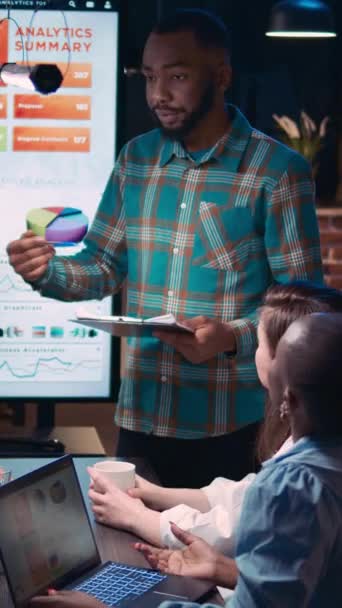 Verticale video: Afro-Amerikaanse man geeft financiële rapport presentatie, werknemer houdt klembord in coworking ruimte. Diverse collega 's bespreken analytics data, praten in zakelijke bijeenkomst op - Video