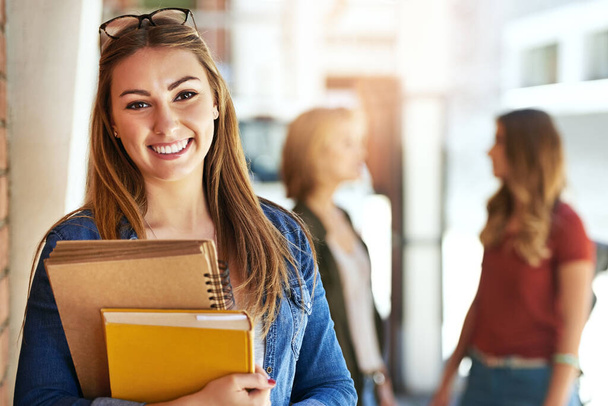 Si distingue per il college. Ritratto di una studentessa sorridente in piedi nel campus con gli amici sullo sfondo - Foto, immagini