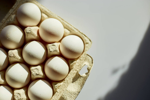 Scatola di cartone con uova bianche su sfondo bianco, luce solare dura, prodotto confezionato con uova biologiche. - Foto, immagini