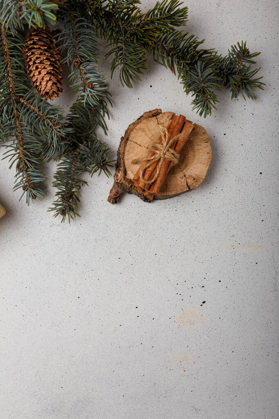 Blue fir tree branch with cone, wooden cut and cinnamon sticks on white wooden background. Christmas card, copy space, vertical shot - 写真・画像
