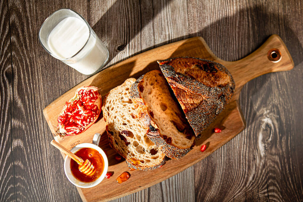 Miel, granada, leche y pan en una tabla de cortar de madera. Vista desde arriba. - Foto, imagen