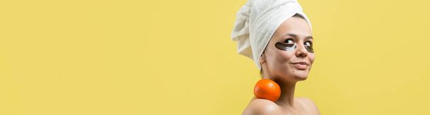 Beauty portrait of woman in white towel on head with gold nourishing mask on face. Skincare cleansing eco organic cosmetic spa relax concept. A girl stands with her back holding an orange mandarin. - Фото, зображення