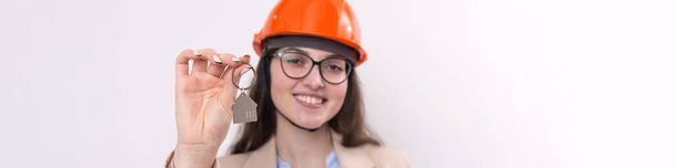 A girl in a construction helmet holds a house. Realtor on a white background. - Фото, зображення