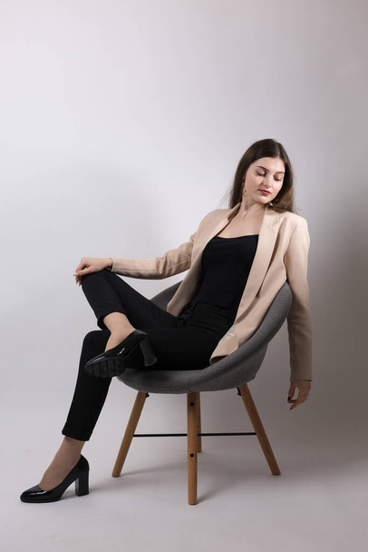 Retrato de una joven morena de pelo largo en el estudio. Linda chica sentada en una silla sobre un fondo blanco. - Foto, Imagen