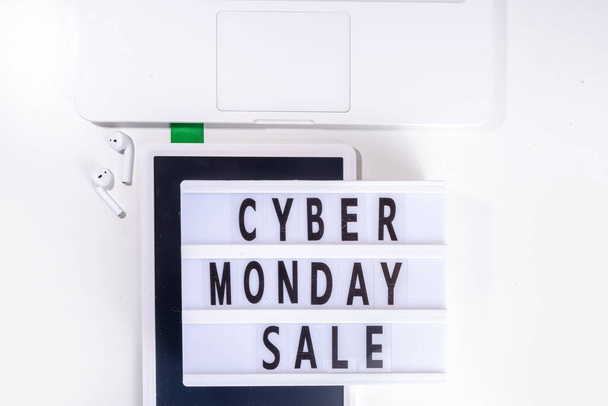 Cyber monday sale background. Simple white flat lay with lightbox "Cyber monday", gift boxes, shopping cart, laptop, tablet, headphones top view copy space. Online holiday shopping concept - Photo, image