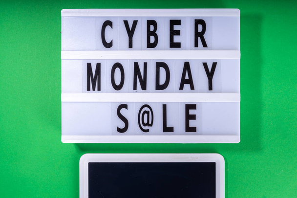 Cyber monday sale background. Simple bright green flat lay with lightbox "Cyber monday", gift boxes, shopping cart, laptop, tablet, headphones top view copy space. Online holiday shopping concept - Fotó, kép