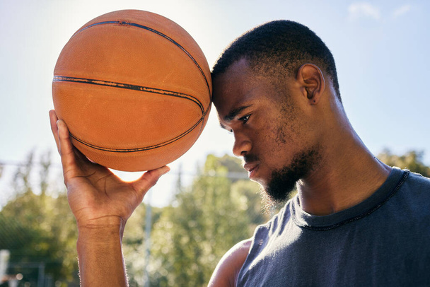 Basketball on forehead, motivation and black man on basketball court ready for competition, match or game. Basketball player, sports and male from Nigeria preparing for training, fitness or exercise - Photo, image