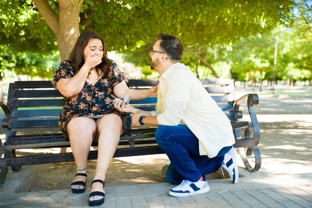 Vriendje op zijn knieën vraagt zijn vriendin ten huwelijk en verrast haar met een verlovingsring in het park - Foto, afbeelding
