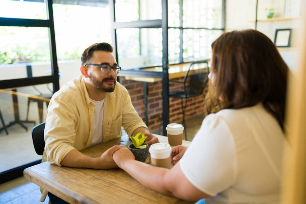 Bello giovane uomo che si tiene per mano con la sua ragazza grassa mentre ha un appuntamento in una caffetteria - Foto, immagini