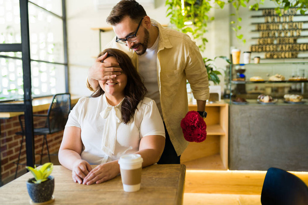 Adorable boyfriend covering the eyes of his girlfriend to surprise her with flowers during a coffee date - Φωτογραφία, εικόνα