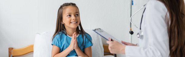 Fille faisant s'il vous plaît geste près de pédiatre avec presse-papiers à la clinique, bannière  - Photo, image