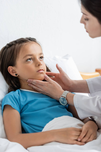 Médecin flou examinant le cou d'un enfant sur un lit d'hôpital  - Photo, image