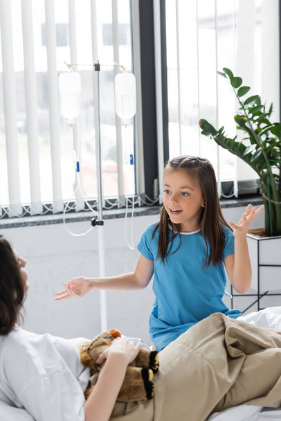 Dziewczyna rozmawia z niewyraźną mamą w pobliżu terapii dożylnej na oddziale szpitalnym  - Zdjęcie, obraz