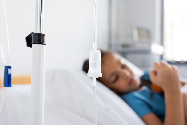 Terapia intravenosa en pie cerca de un niño enfermo borroso en el hospital  - Foto, imagen