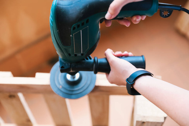 Close-up of two hands of an unrecognizable woman sanding a pallet with an electric sander. Home renovation - Photo, Image