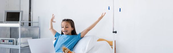 Enfant excité en robe de patient regardant ordinateur portable dans la salle d'hôpital, bannière  - Photo, image