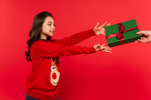 cheerful girl in winter sweater taking wrapped Christmas present from father on red - Φωτογραφία, εικόνα