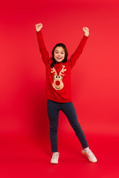 full length of amazed child in sweater and jeans gesturing on red - Фото, изображение