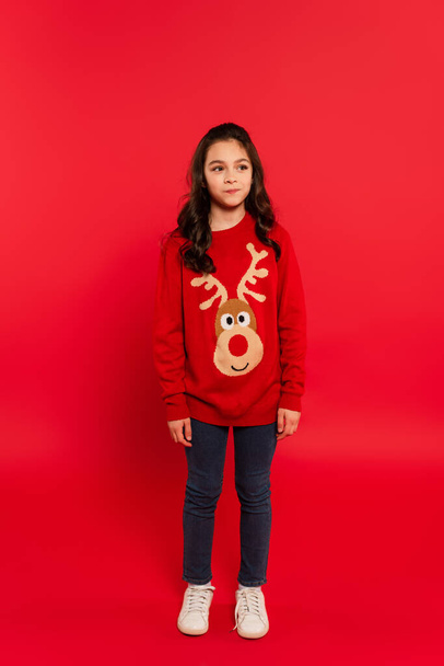 full length of puzzled kid in winter sweater looking away on red - Фото, изображение