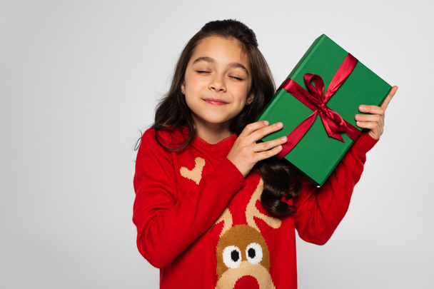 Pleased child in red sweater holding Christmas gift isolated on grey  - Fotografie, Obrázek