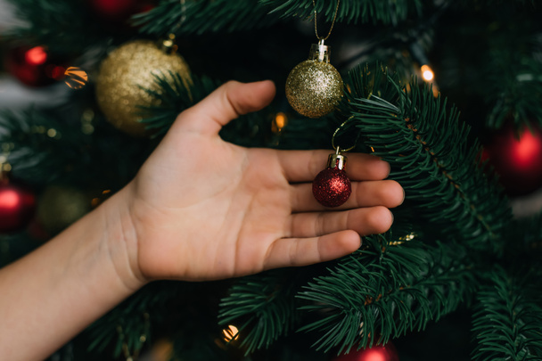 Vue recadrée d'un enfant touchant une boule brillante sur un arbre de Noël  - Photo, image
