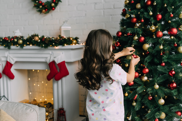 Bambino in pigiama che addobba l'albero di Natale in salotto  - Foto, immagini