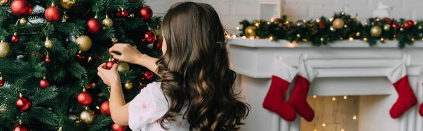 Preteen dítě zdobení vánoční stromeček u rozmazaného krbu doma, prapor  - Fotografie, Obrázek