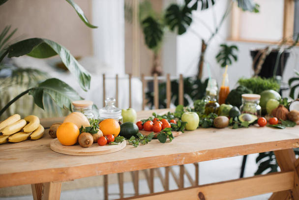 Prepared fruits, tomatoes, bananas, oranges, avocados, apples, mint, coconuts, greens, vegetables, to make salad, smoothies for morning healthy eating lying on wooden table in tropical exotic kitchen - Photo, Image