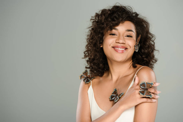 joyful african american woman with butterflies on body and cheek posing isolated on grey  - Fotografie, Obrázek