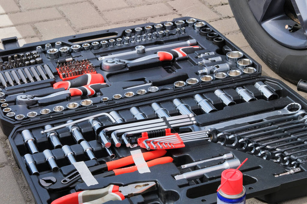 Tool set in box near the orange auto. Different tools for repairing and diagnostic a car. Automobile maintenance concept. - Photo, Image