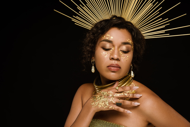 young african american woman with golden accessories and paint on hand posing isolated on black - Photo, Image