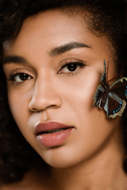 close up of curly african american woman with butterfly on face looking at camera - Fotografie, Obrázek