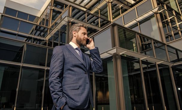 серьезный успешный бородатый бизнесмен в официальном костюме выступая на смартфоне, телефон ответ. - Фото, изображение