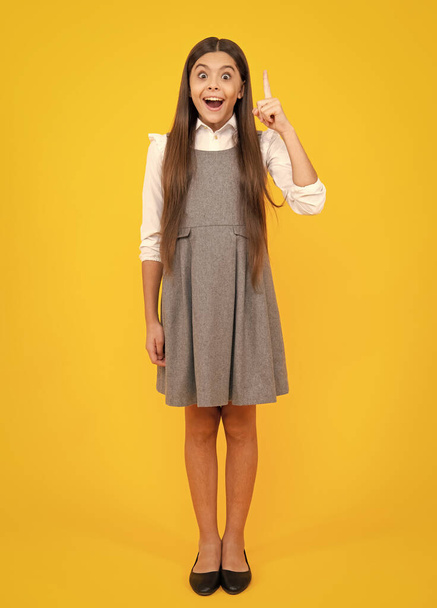 Close up funny face of young teenager pointing up with finger, isolated on yellow background. Girl has great new idea. Successful child. Excited face. Amazed expression, cheerful and glad - Fotó, kép