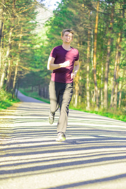 Running man jogging in city park at beautiful summer day. Sport fitness model caucasian ethnicity training outdoor. - 写真・画像