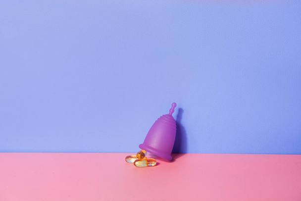 Weibliche Menstruationstasse und Ölkapseln auf rosa Tisch. Konzept zum Wohlergehen der Frau   - Foto, Bild