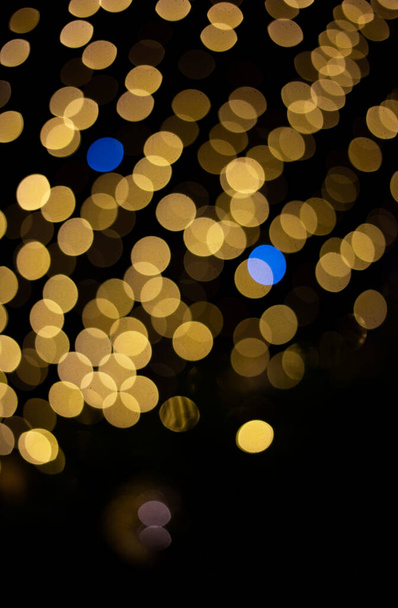 defocused Christmas holiday lights from garlands of yellow and a few blue ones. Abstract festive background, bokeh. Ukrainian flag colors - Photo, Image