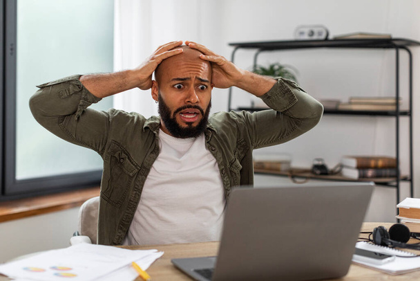 Oh no, error concept. Shocked mature latin man using pc, gasping with open mouth and grabbing his head, sitting at desk at home. Stressed male suffering business problems or reading bad news - Photo, Image