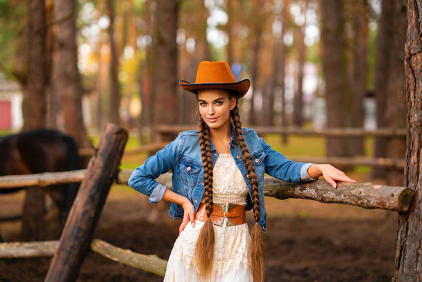 Portrait of a beautiful cowegirl with extra long braided hair and vintage dress in the countryside, posing in the forest. - Foto, Imagen