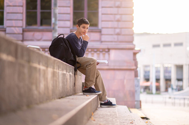 Cute dark-haired teenage boy with an open book in the hand staring into the distance - Fotó, kép