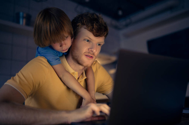 Togetherness. Ginger man nad his cute son watching something on internet in the evening - Foto, imagen