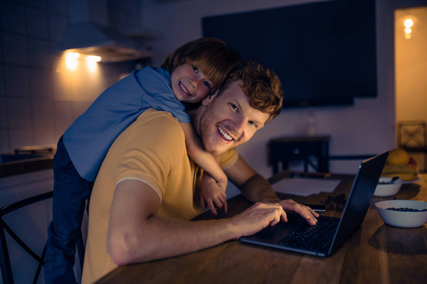 Togetherness. Ginger man nad his cute son watching something on internet in the evening - Foto, afbeelding