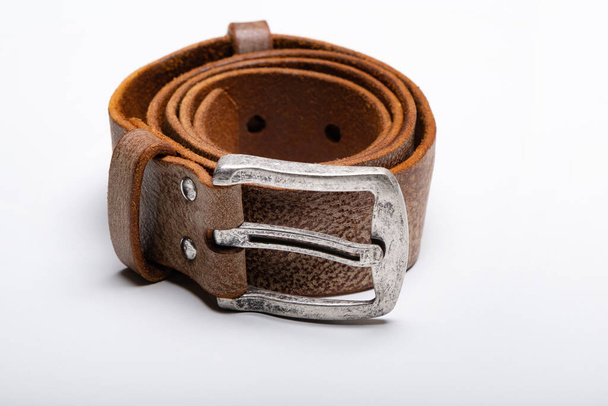 Un cinturón de cuero marrón enrollado con una hebilla de metal en una mesa blanca. Copiar espacio - Foto, Imagen