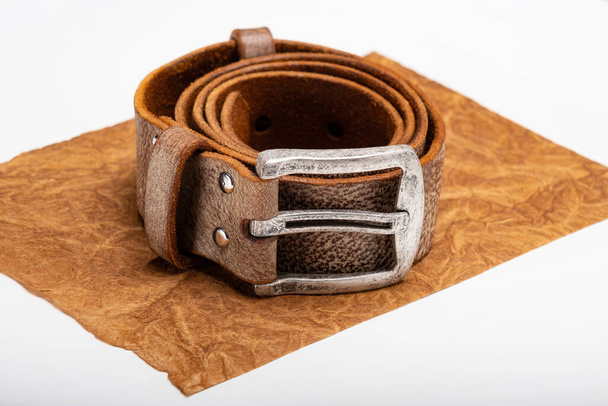 Cintura arrotolata in pelle marrone con fibbia in metallo su un tavolo bianco. Copia spazio - Foto, immagini