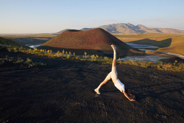 Een jonge vrouw staat in een yoga pose tegen het prachtige natuurlandschap van vallei, vulkanisch meer en krater - Foto, afbeelding