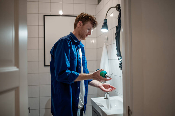 Washing hands. Man in dark-blue shirt in the bathroom washing hands - Fotografie, Obrázek