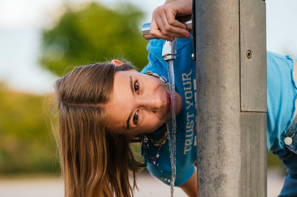 Очень счастливая девушка пьет воду у фонтана в городском парке. - Фото, изображение