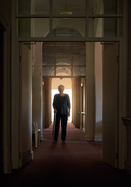 Cuerpo ágil, mente ágil. Retrato de una mujer mayor feliz caminando por un pasillo con su bastón - Foto, imagen