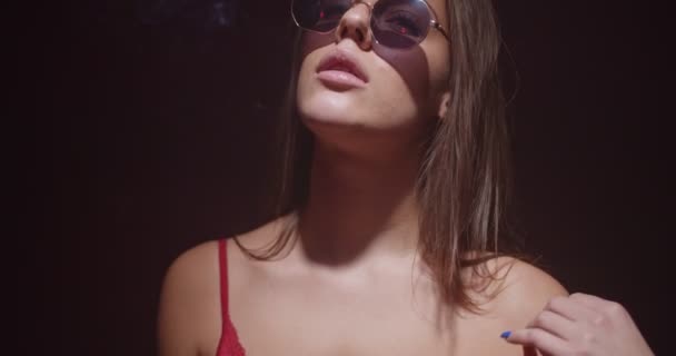 Крутая девушка танцует соблазнительно и курит сигарету в красном нижнем белье с дымом течет изолированы на черном, замедленной съемки - Кадры, видео